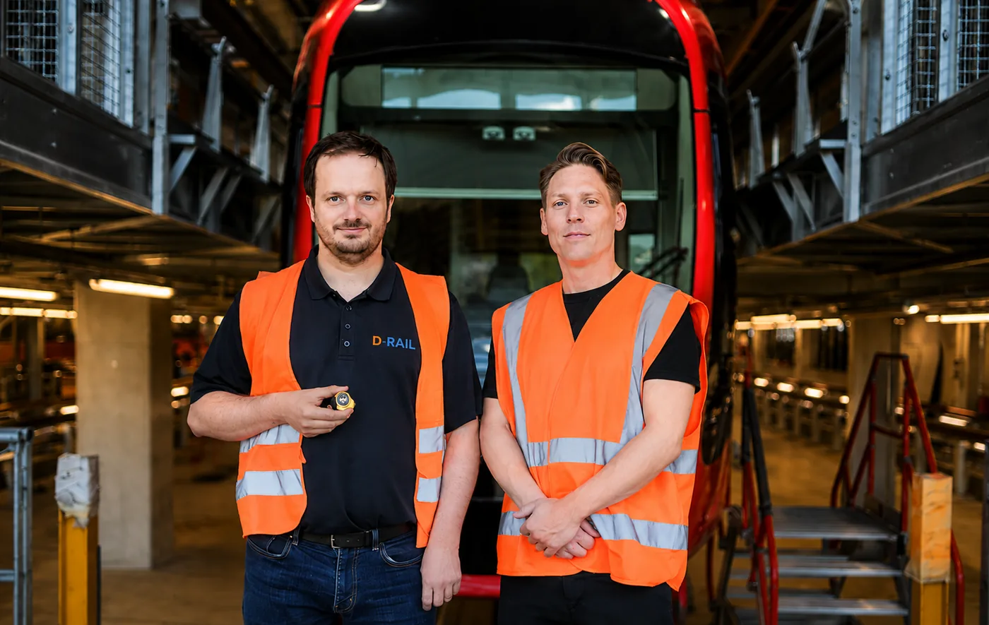 Two D-RAIL engineers in a tram depot, one holding a sensor unit.